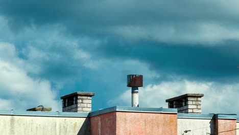 Time-lapse-of-beautiful-white-fast-moving-storm-clouds-behind-the-chimneys-on-the-rooftop,-city-skyline-on-a-sunny-summer-day,-distant-medium-shot