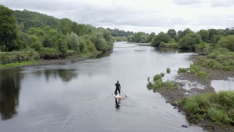 Lone-man-paddles-SUP-on-small-peaceful-river-in-rural-countryside