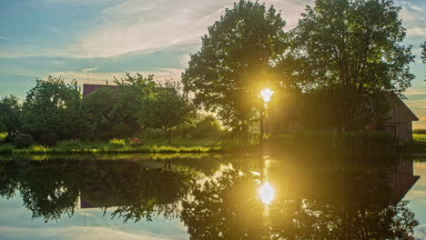 Zeitrafferaufnahme-Des-Sonnenuntergangs-über-Dem-Flusswasser,-Das-Neben-Holzhäusern-Im-Hintergrund-Vorbeizieht