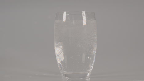 Eiswürfel-Fallen-In-Glas-Mit-Sprudelndem-Wasser-Vor-Weißem-Studiohintergrund