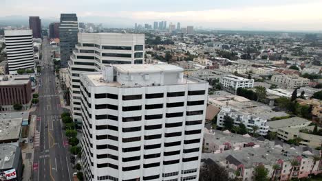 Buildings-in-the-Brentwood-area-of-Los-Angeles-along-Wilshire-Boulevard---ascending-aerial-view-on-a-hazy-morning-with-the-city-skyline-in-the-distance