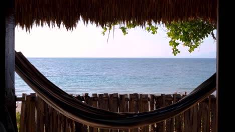 Eine-Hängematte,-Die-In-Der-Brise-Schaukelt-Und-Von-Einer-Traditionellen-Strandhütte-Auf-Einem-Abgelegenen-Urlaubsziel-Auf-Einer-Tropischen-Insel-Aus-Einen-Wunderschönen-Blick-Auf-Das-Meer-Bietet