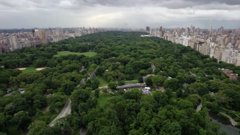 Aerial-view-over-the-Central-park,-revealing-the-Wollman-Rink,-in-cloudy-NYC,-USA---tilt,-drone-shot