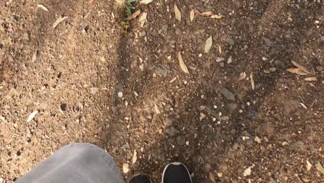 Looking-down-at-a-man's-feet-in-black-runners-walking-along-a-dirt-trail