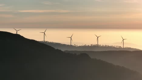 Rotierende-Windkraftanlagen-Auf-Waldbedeckten-Hügeln-Bei-Sonnenuntergang-In-Portugal