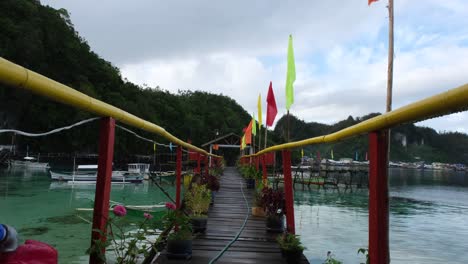 Hanging-mini-bridge-on-the-water-with-a-colorful-flag-and-a-sea-with-boats-in-the-background