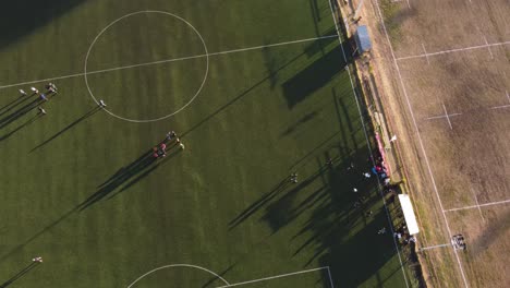 Top-down-aerial-view-of-soccer-field-with-players-at-sunset