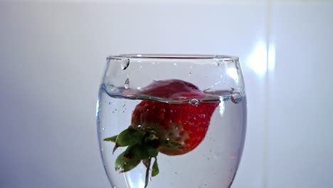 Strawberry-dropped-into-a-wineglass-of-liquid-in-slow-motion-against-a-white-background