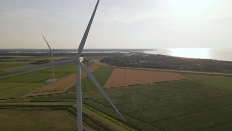Static-drone-footage-of-two-rotating-wind-turbines-near-the-flat-coastline-of-south-west-holland,-europe