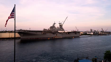 Aerial-View-Of-Aircraft-Carrier-Docked-At-General-Dynamics-Nassco-Shipyard-In-Norfolk,-Virginia-With-Purple-Sunset-Skies