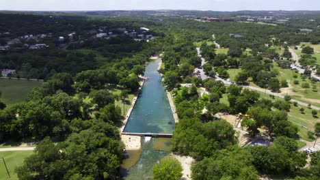 Aerial-view-away-from-the-Barton-Springs-Municipal-Pool,-sunny,-summer-day-in-Austin,-USA---reverse,-tilt,-drone-shot