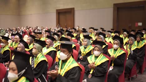 Happy-graduates-in-hats-and-robes-siting-in-row-and-applauding