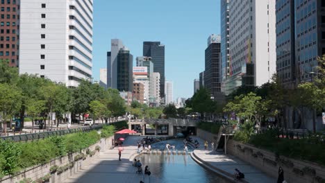 Seoul-Urban-Cheonggyecheon-Stream-Park-with-Large-Groups-of-People-Traveling-and-Resting-by-the-Waving-River-on-Summer-Beautiful-Day,-South-Korea