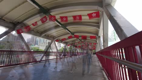 Busy-pedestrian-bridge-decorated-with-Hong-Kong-and-China-flags,-time-lapse