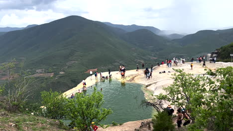 Panoramic-Dolly-View-of-Natural-Thermal-Site-on-Top-of-Mountain,-Hierve-El-Agua,-San-Lorenzo-Albarradas,-Oaxaca-Mexico,-Tourists-Visiting-Refreshing-at-Mineral-Waters-Basin-Pool-at-Edge-of-Mountain