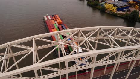 Aerial-View-Through-Bridge-Over-The-Noord-Of-Maas-Push-Tow-Barge-Carrying-Cargo-Containers-Along-River-Passing