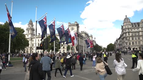 Crowds-Of-People-Walking-Across-Parliament-Street-Square-With-Commonwealth-Flags-Waving-In-Wind