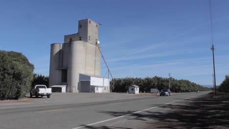 cars-drive-by-a-large-grain-silo-in-Butte-County-California-Almonds,-corn-production-in-4k