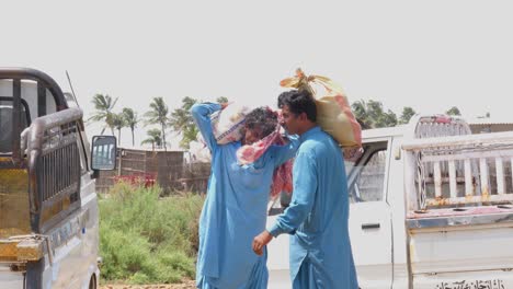 Dos-Hombres-Paquistaníes-Sosteniendo-Sacos-Sobre-Sus-Hombros-Afuera-Durante-Un-Campamento-De-Inundaciones-En-Un-Día-Soleado