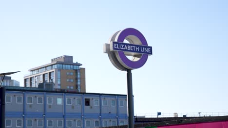 Canary-Wharf,-London,-United-Kingdom---August-2022---A-pole-and-sign-of-the-new-Elizabeth-Line-in-purple-color-during-a-beautiful,-clear,-sunny-morning-in-Canary-Wharf