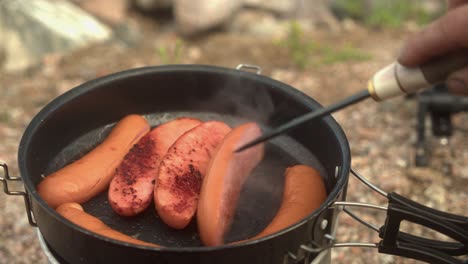 Frankfurter-sausages-are-flipped-in-frying-pan-on-hot-outdoor-stove