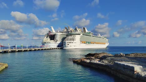 Luxury-cruise-ships-docked-next-to-each-other-in-port-of-Nassau,-Bahamas-|-Luxury-cruise-ships-Owned-and-operated-by-Royal-Caribbean-International-|-People-disembarking-on-pier-on-island,-Vacation