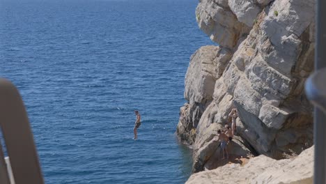 Young-caucasian-male-jumping-off-rocky-cliffs-in-Old-town-Dubrovnik,-Croatia