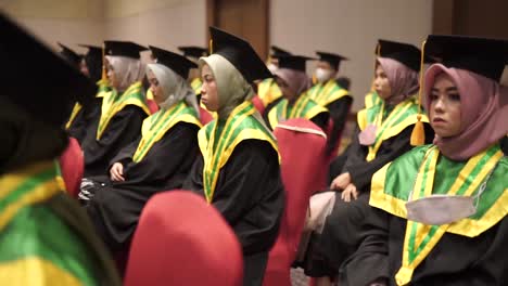 College-students-dressed-in-cap-and-gowns-listen-to-a-speech-during-a-graduation-ceremony