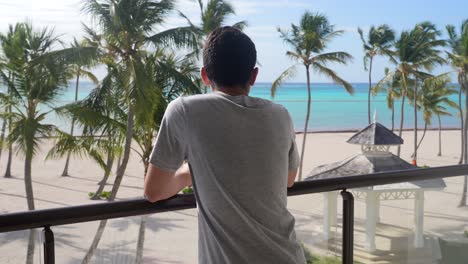 Ein-Junger-Erwachsener-Mann-Blickt-Vom-Balkon-Seines-Zimmers-Auf-Den-Karibischen-Strand