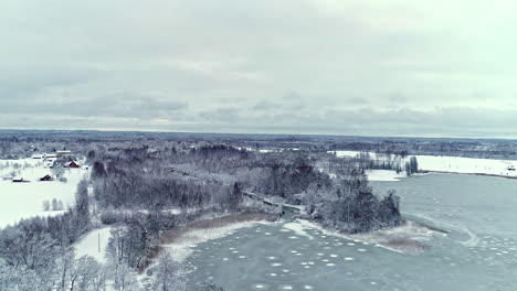 A-frozen-lake,-snow,-and-frosty-evergreen-forest-on-a-cold-winter-day---aerial-flyover