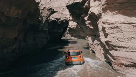 Offroad-SUV-Jeep-Renegade-Longitude-driving-in-canyon-river,-aerial-follow-shot