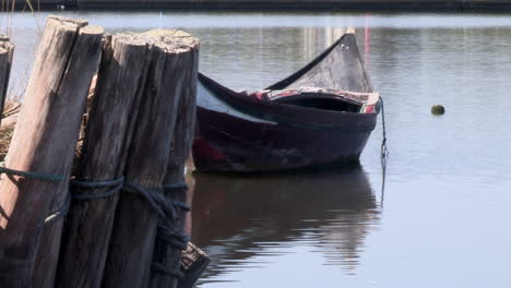 Small-wooden-boat-moored-in-the-river,-logs-upright-to-hold-the-riverbanks