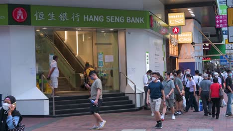 Chinesische-Fußgänger-Gehen-An-Dem-In-Hongkong-Ansässigen-Bank--Und-Finanzdienstleistungsunternehmen-Und-Dem-Hauptindikator-Für-Den-Hongkonger-Aktienmarkt,-Der-Hang-Seng-Bank-Und-Einer-Filiale-In-Hongkong-Vorbei