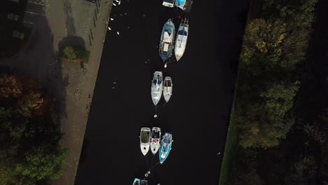 Descending-shot-over-boats-on-canal,-bird-flies-through-right-of-shot