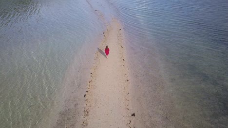 Aerial-tracking-shot-of-young-brunette-woman-in-red-dress-walking-on-sandbar-in-Asia-away-from-camera