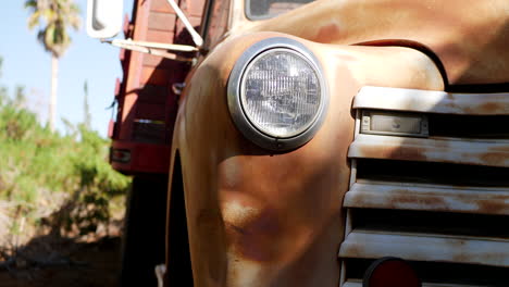 Dropping-down-along-the-front-of-an-old-rusty-vintage-truck-fender-with-glass-headlight-and-grill-in-the-sunlight
