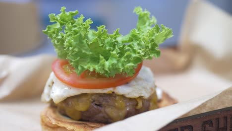 Nahaufnahme-Eines-Gourmet-Cheeseburgers-Mit-Tomate-Und-Der-Chefkoch-Fügt-Salat-Und-Das-Obere-Brötchen-Hinzu