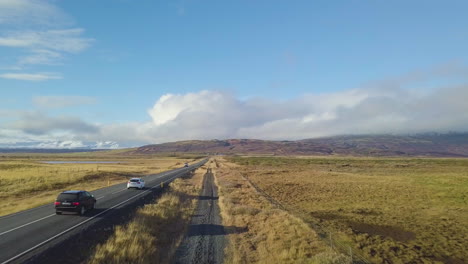 Vista-De-Drones-De-Caminos-De-Tierra-Y-Carreteras-Con-Vehículos-Al-Lado-De-Campos-Y-Tierras-De-Cultivo-Con-Montañas-Al-Fondo
