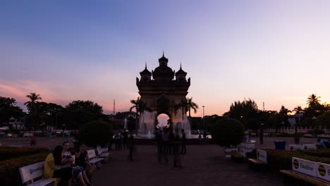 Patuxai-monument-lighting-up-at-sunset,-Vientiane-with-people-in-foreground