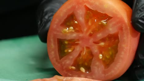 Close-up-of-gloved-hands-cutting-a-tomato-into-slices