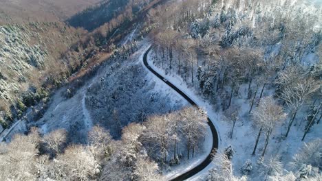 Aerial-view-of-Cars-driving-on-curvy-winter-country-road-in-snowy-forest