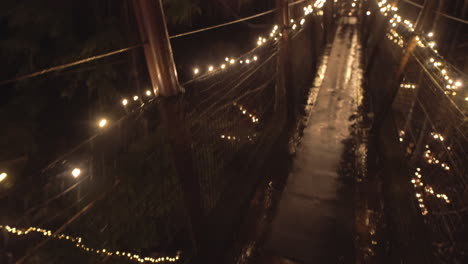 Elevated-suspension-bridge-in-treetop-decorated-with-Christmas-lights,-Rainy-night