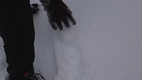 A-hand-with-a-glove-on-is-seen-rolling-a-snowball-across-the-ground-in-slow-motion