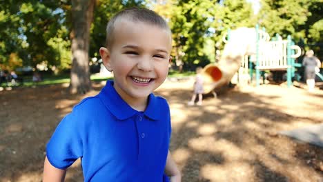 Mischievous-blonde-boy-in-blue-shirt-laughing-in-the-sunshine-at-the-park
