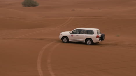 Wide-shot-of-a-vehicle-drives-in-the-sahara-desert,-Dubai,-UAE