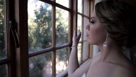 Bride-walks-up-to-the-window-and-looks-out-as-she-dreams-about-her-wedding-that-is-about-to-happen