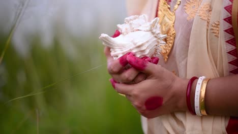 The-hands-of-a-newly-wed-Indian-woman-wearing-saree-holding-a-shankha-or-conch-shell-in-a-field-outdoor