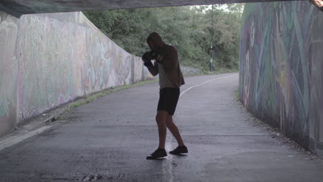 Young-Active-Man-Boxing-In-Underpass,-Silhouetted-By-Light