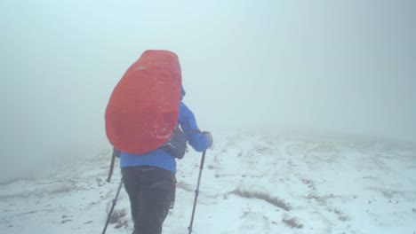 rocky-alpine-peaks,-landscape-of-a-slovakian-tatra-mountains,-slow-motion-handheld-shot-following-a-female-hiker-walking-on-a-trail-in-a-snowstorm