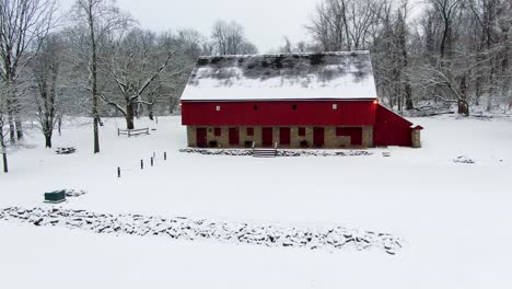 Aerial-revealing-shot-of-red-barn-on-Rock-Ford-Plantation-in-Winter,-home-to-General-Edward-Hand,-winter-landscape-with-fresh-snow,-travel-concept,-heritage-sites